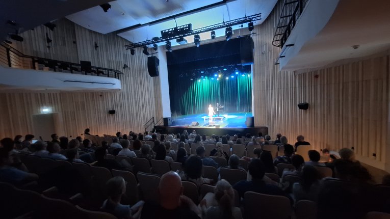 Pełna sala publiczności, w tle scena.