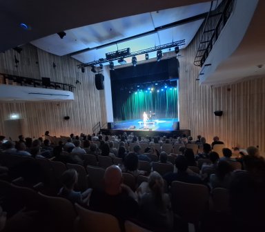 Pełna sala publiczności, w tle scena.