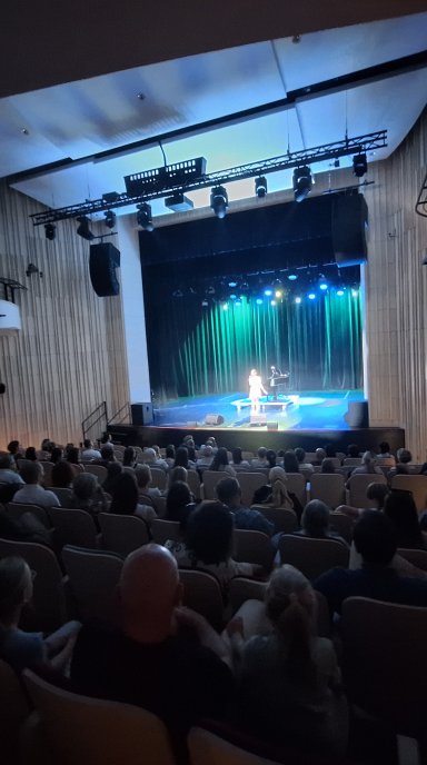 Pełna sala publiczności, w tle scena.