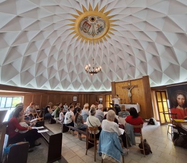 Uczestnicy warsztatów Gospel ćwiczą pod okiem dyrygentki w sali z kopułą.